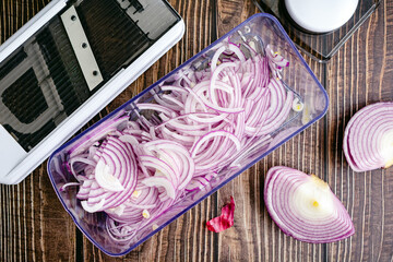 Red Onions Sliced Thinly with a Mandoline: Thinly sliced red onion and a mandoline viewed from...