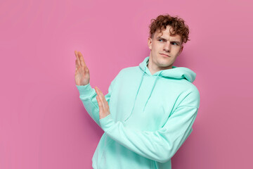 curly guy in mint hoodie pulls away and refuses on pink isolated background, man ignores and avoids...