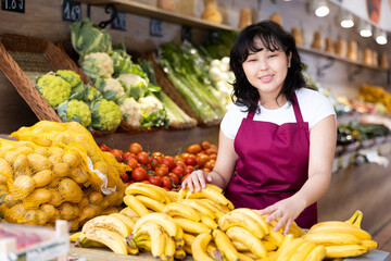 Smiling young saleswoman posing happily in front of counter in grocery store with large assortment