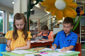 Cute girl and boy sit and draw together in preschool institution