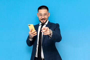hey you. successful asian businessman in suit and glasses uses smartphone and points chooses you