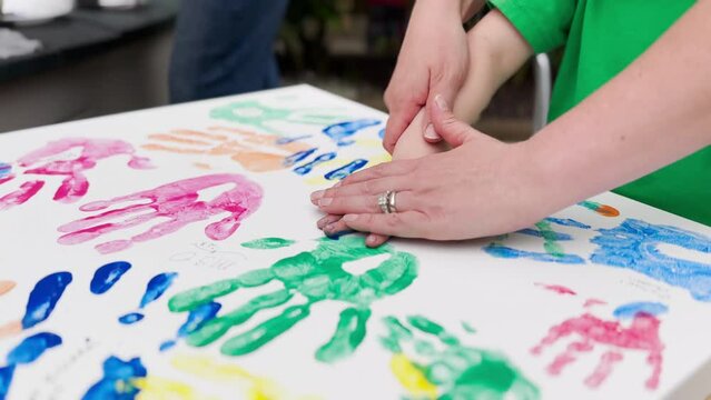 A little boy gets help from his mom putting his handprint on a painting canvas at a backyard family birthday party.	