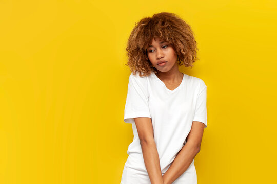 young insecure curly american girl is sad and bored over yellow isolated background