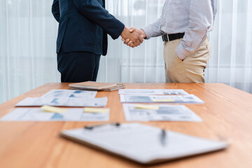 Two businesspeople shake hand after signing contract document to merge their partnerships in conference room and finalized pile of papers of financial report and data analysis on meeting table. Entity - obrazy, fototapety, plakaty