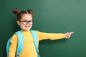 Happy little school child with backpack pointing at chalkboard
