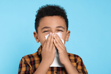 African-American boy blowing nose in tissue on turquoise background. Cold symptoms - Powered by Adobe