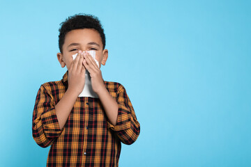 African-American boy blowing nose in tissue on turquoise background, space for text. Cold symptoms - Powered by Adobe