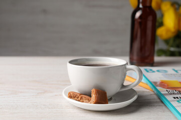 Cup of aromatic coffee, caramel candies and syrup on white wooden table