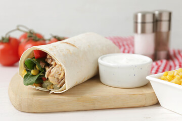 Delicious tortilla wrap with tuna and sauce on white wooden table