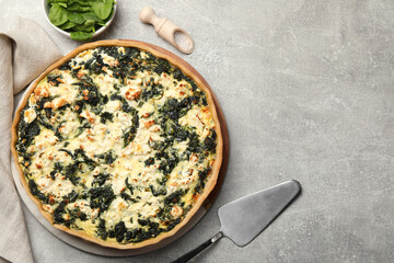 Delicious homemade quiche, fresh spinach leaves and spatula on light gray table, flat lay. Space for text