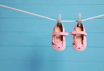 Obraz premium Pink baby shoes drying on washing line against light blue wooden wall. Space for text