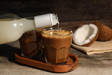 Fototapeta Pouring coconut syrup into glass with tasty coffee at wooden table, closeup obraz