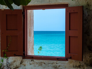 View of Tropical Waters on a Sunny Day Through a Window of an Abandoned Building with Shutters Looking out to Paradise
