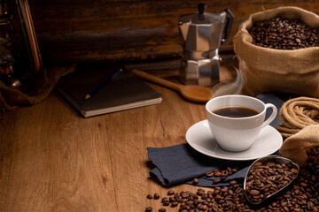 coffeeHot coffee in a white coffee cup and many coffee beans placed around on a wooden table in a warm, light atmosphere, on dark background.