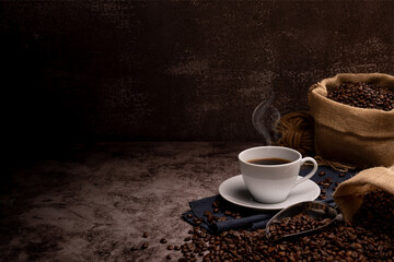 coffeeHot coffee in a white coffee cup and many coffee beans placed around on a wooden table in a warm, light atmosphere, on dark background.