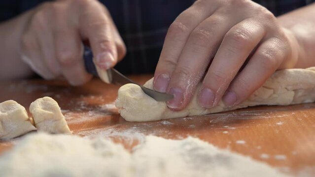 Hand with a knife confidently cuts pieces of kneaded dough on a table with flour. Homemade baking recipe, handmade noodles preparation. Cook teaches how to cook pastries, a master class on bread