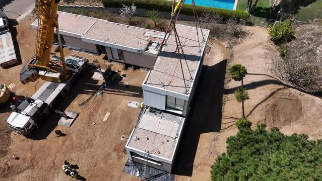 Heavy crane lifting modular home building piece, aerial orbit view