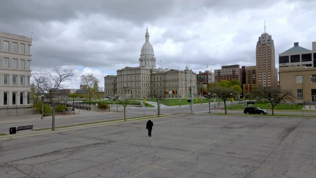 Man walking towards the Michigan State Capitol building in Lansing, Michigan with wide shot drone video following.