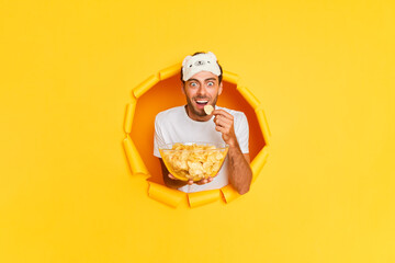 Young bearded guy in white tshirt is very excited while looking movie with crisps, posing on yellow background, enjoyment concept, copy space