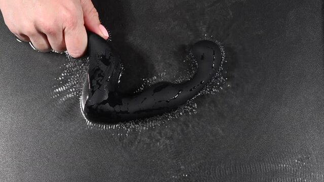 A woman holds a black prostate stimulator that vibrates and creates ripples on the surface of the water against a black background.