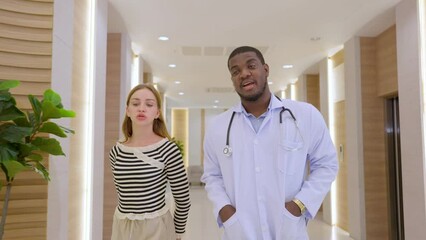 Caucasian doctor walk in hallway with patient's relative in hospital. 