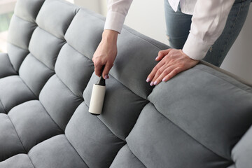 Woman uses roller to remove pellets from grey soft couch