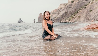 Woman summer travel sea. Happy tourist in black dress enjoy taking picture outdoors for memories. Woman traveler posing on sea beach surrounded by volcanic mountains, sharing travel adventure journey