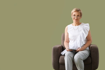 Mature psychologist with tablet computer sitting in armchair on green background