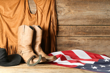 Cowboy hat, boots and flag of USA on wooden background