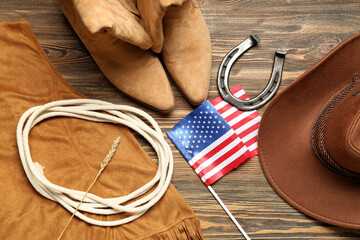 Composition with different cowboy accessories and flag of USA on brown wooden background