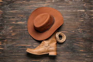 Cowboy hat, boots and lasso on brown wooden background