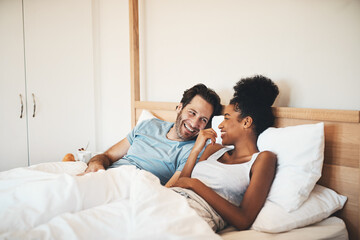 Interracial couple, laughing and relax on bed for morning bonding, funny relationship or joke at home. Happy woman and man with smile, laugh and lying in bedroom for fun talk or conversation indoors
