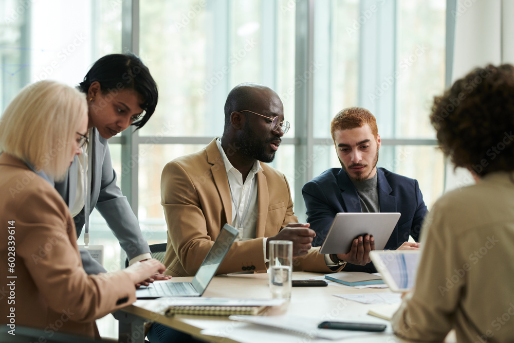 Poster Confident analyst with tablet explaining online data to colleague during discussion of financial graphs and charts among coworkers in office