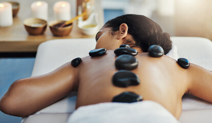 Obraz na płótnie Canvas Woman, relax and rock massage at spa for skincare, beauty or body treatment on bed at resort. Calm female lying in relaxation with hot rocks or stone pile on back in therapy, zen or wellness at salon