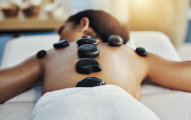 Woman, relax and stone massage at spa for skincare, beauty or body treatment on bed at resort. Calm female lying in relaxation with hot rocks or pile on back in therapy, zen or wellness at salon