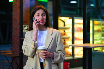 A beautiful woman dressed in casual attire is enjoying a cup of coffee in an urban setting. She...