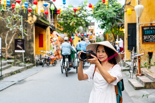 Happy Asian tourist woman wearing Non La (traditional Vietnamese hat) enjoy sightseeing in Hoi An old town Vietnam. Copy space