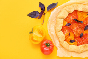 Baking paper with tasty tomato galette and basil on yellow background