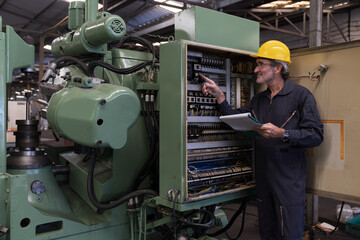 Senior male electrician worker checking, repair, maintenance electric system of CNC machine in factory. Mature male electrician engineer inspecting quality electric during manufacturing process