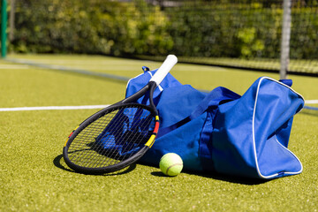 Tennis racket, ball and sports bag on sunny outdoor grass tennis court