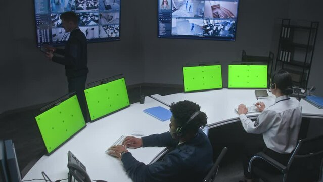 Multiracial officers control security cameras. Workers in monitoring control center. Big digital screens showing surveillance CCTV cameras video footage. Computer monitors with chroma key green screen