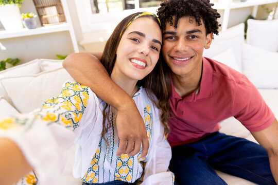Portrait of happy diverse couple smiling for selfie and embracing, sitting in living room at home - Powered by Adobe