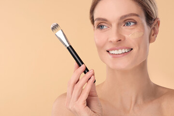 Fototapeta premium Woman with swatch of foundation holding makeup brush on beige background. Space for text