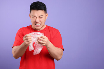 Emotional asian man with bubble wrap on purple background. Space for text