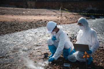 Ecologist sampling water toxic chemicals from river with test tube glass and have white smoke, Biologist wear protective suit and mask collects sample waste water from industrial, problem environment