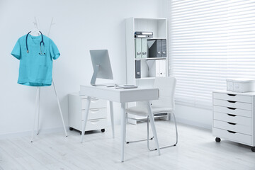 Turquoise medical uniform and stethoscope hanging on rack in clinic