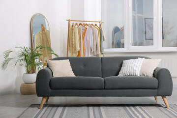 Stylish living room interior with comfortable grey sofa and clothing rack