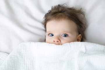 Cute little baby lying under blanket on soft bed, top view