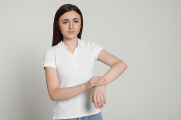 Young woman suffering from pain in her hand on light grey background, space for text. Arthritis symptoms