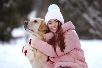 Beautiful young woman hugging cute Labrador Retriever on winter day outdoors
